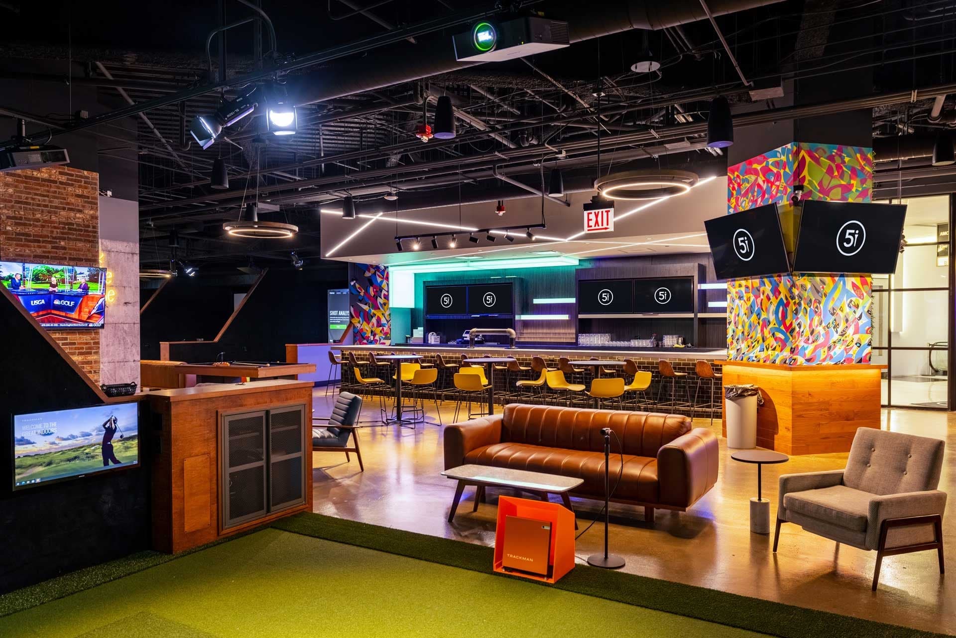 Five Iron Golf Chicago The Loop — The Loop room end-to-end: amber-lit bar with stools, tan leather sofa and armchairs on put