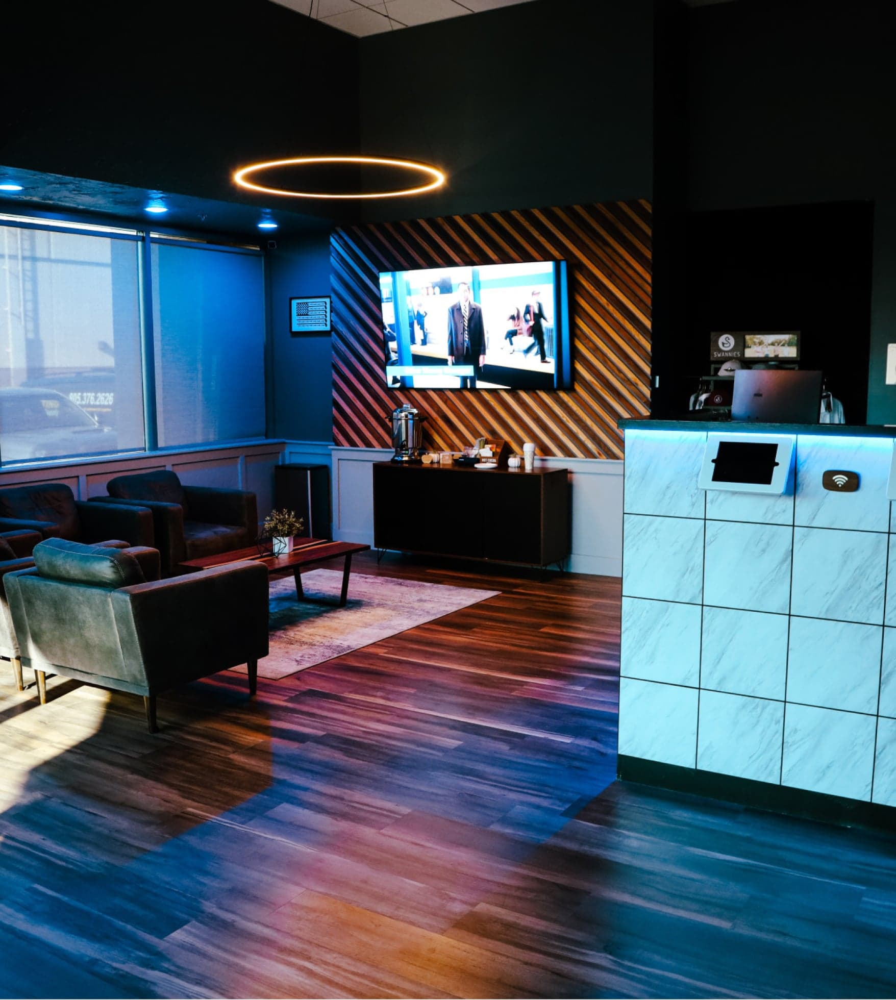 SVN2 Indoor Golf Newbury Park — Lounge: green velvet and black leather armchairs on dark timber, angled wood-slat feature