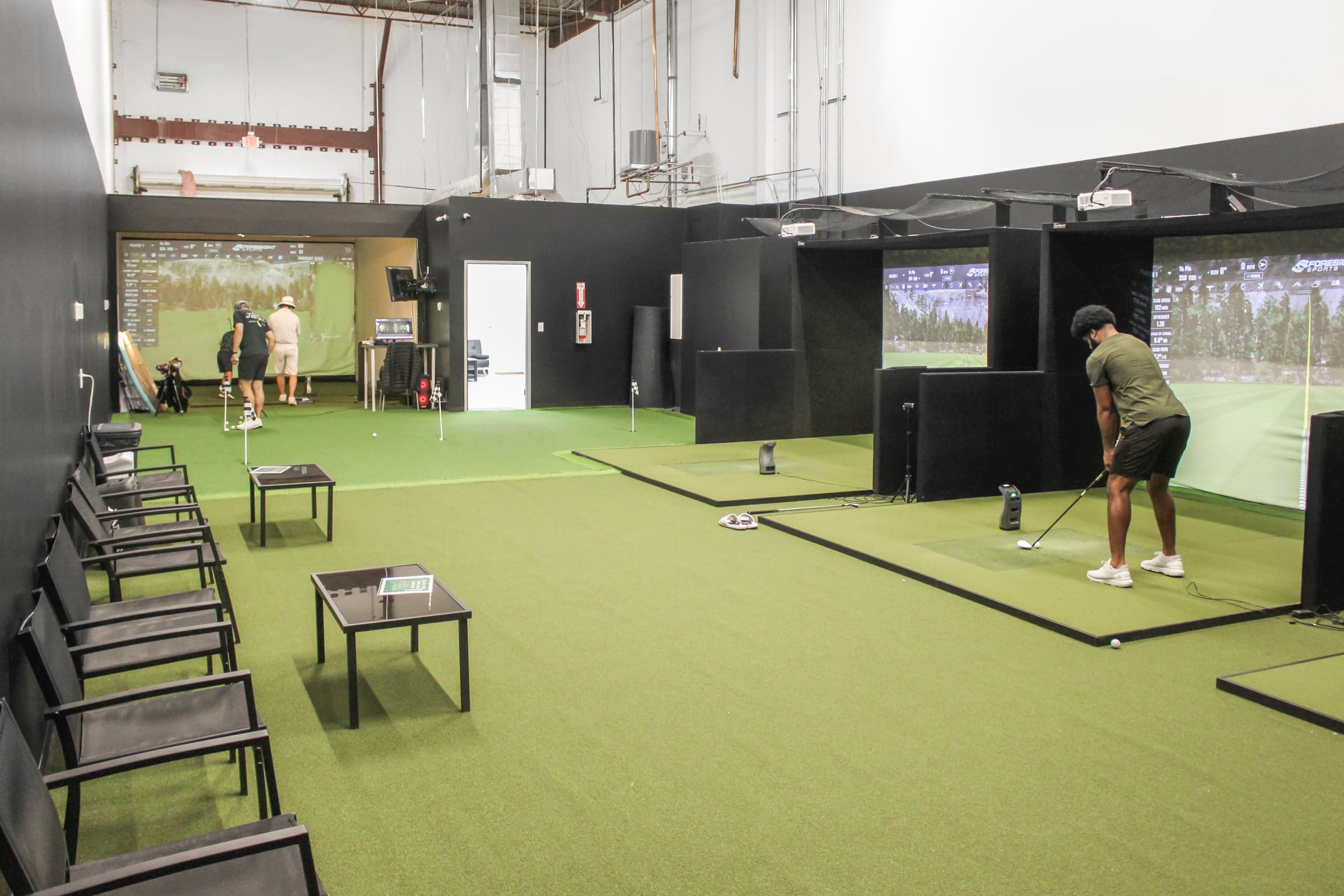 Texas Golf Studio in Houston, TX — Whole studio floor: a row of black-partitioned bays along the right, folding chairs and ta