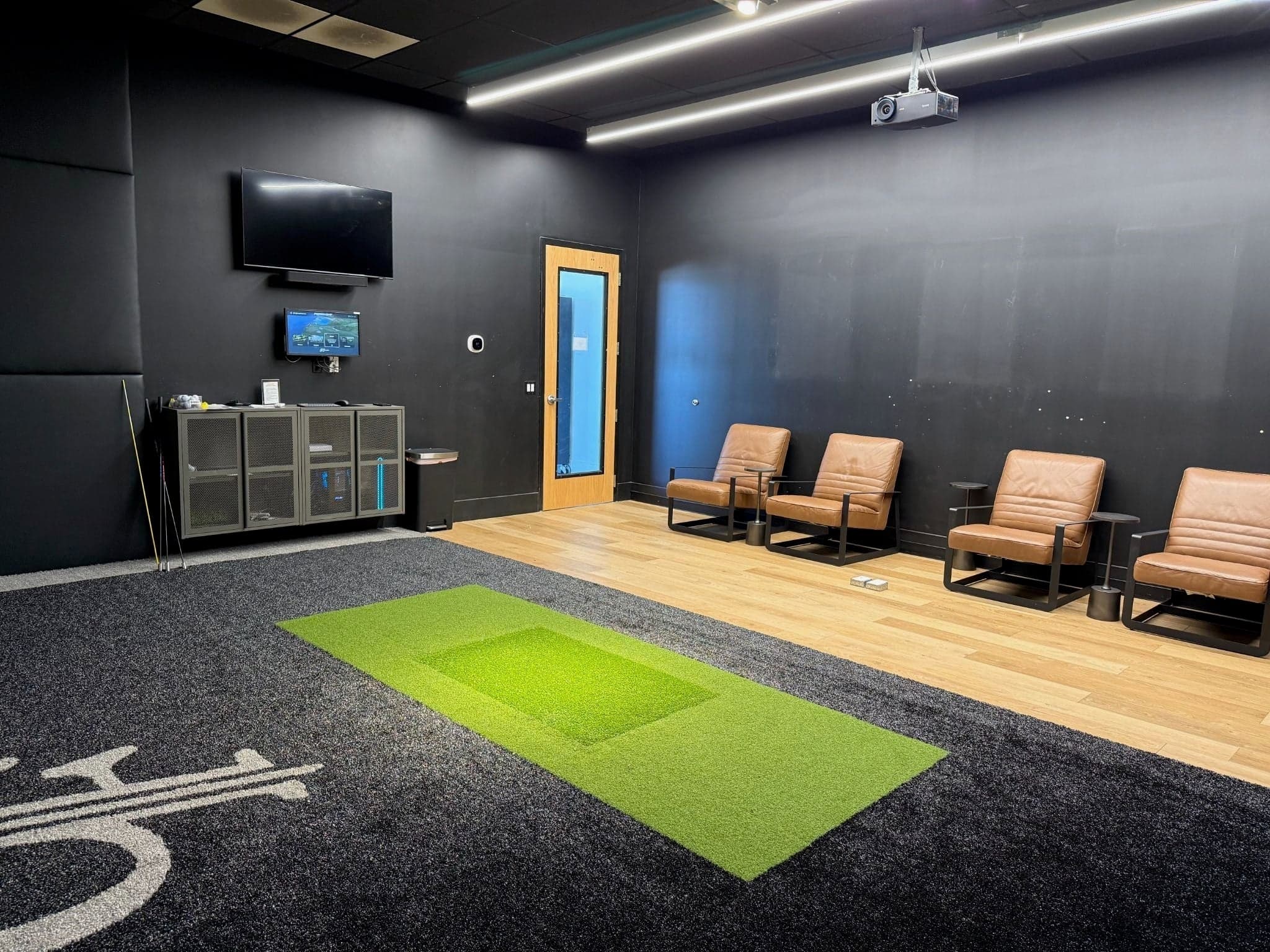 The Golf Forge - South Jordan — Private bay room, lights up: navy walls, four tan leather lounge chairs on pale oak, hitti